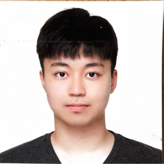 Passport photo of a young man with short dark hair, wearing a dark shirt against a plain background.