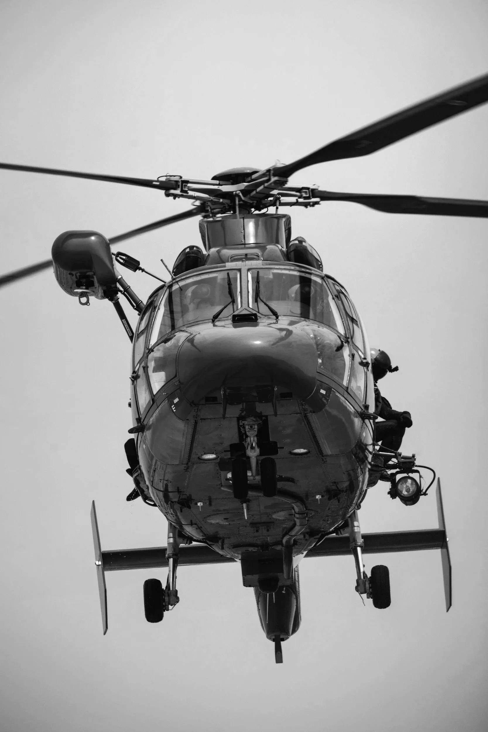 A black and white photo of a helicopter viewed from below, with a clear sky background.
