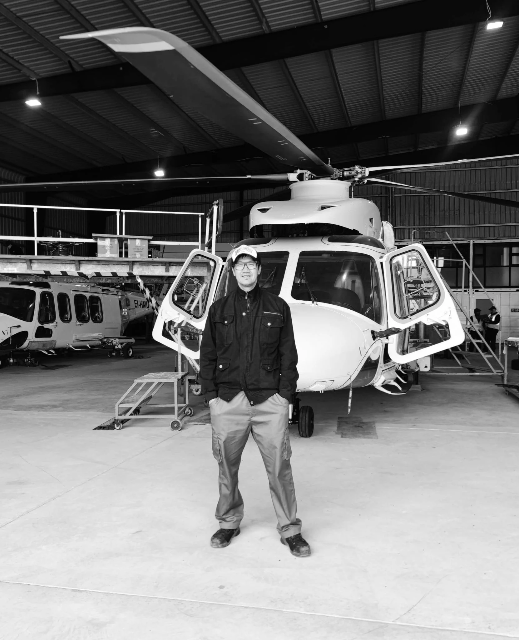 A man standing in front of a helicopter inside an aircraft hangar.