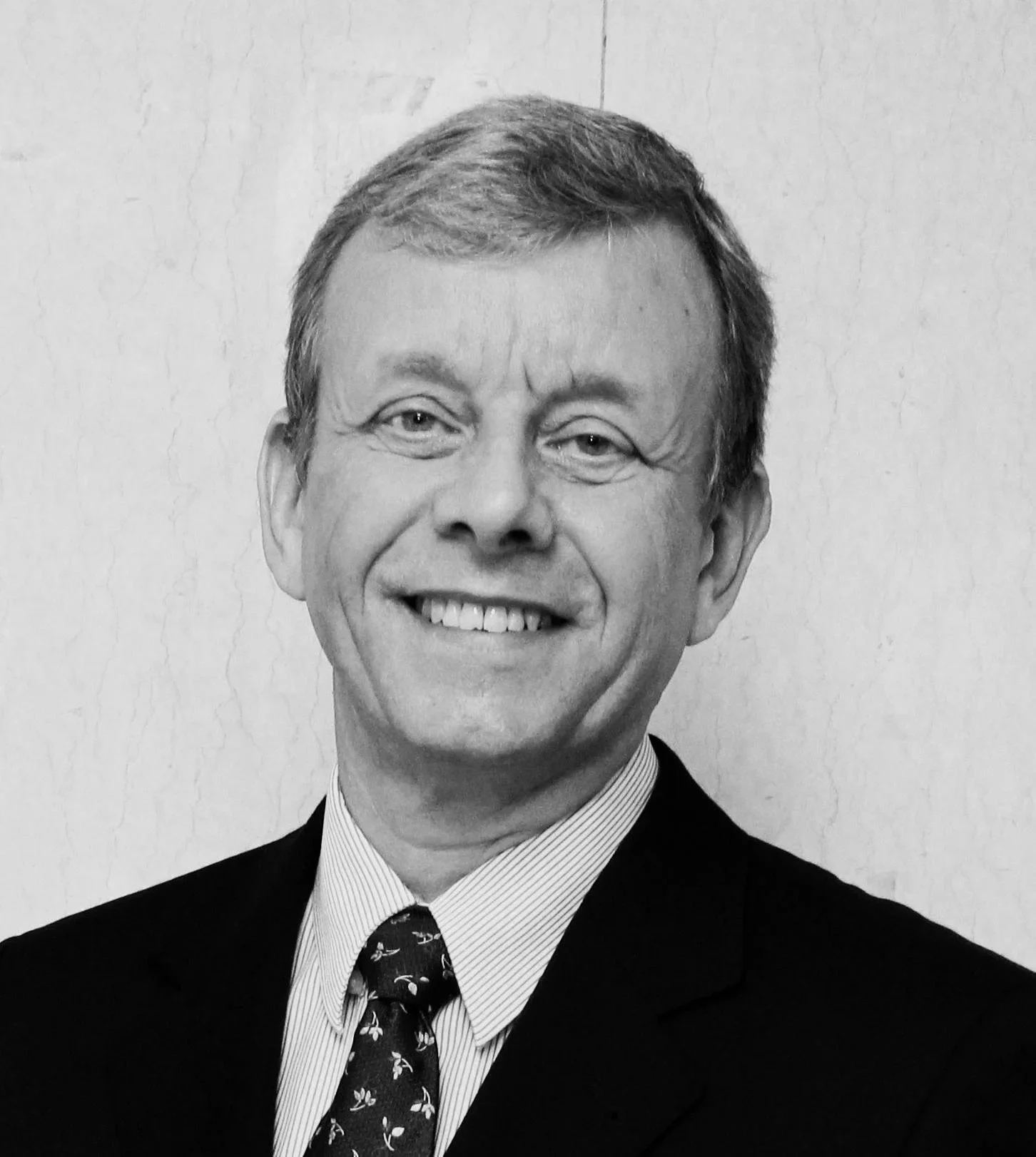 Black and white photo of a smiling middle-aged man in a suit and tie, standing against a plain background.