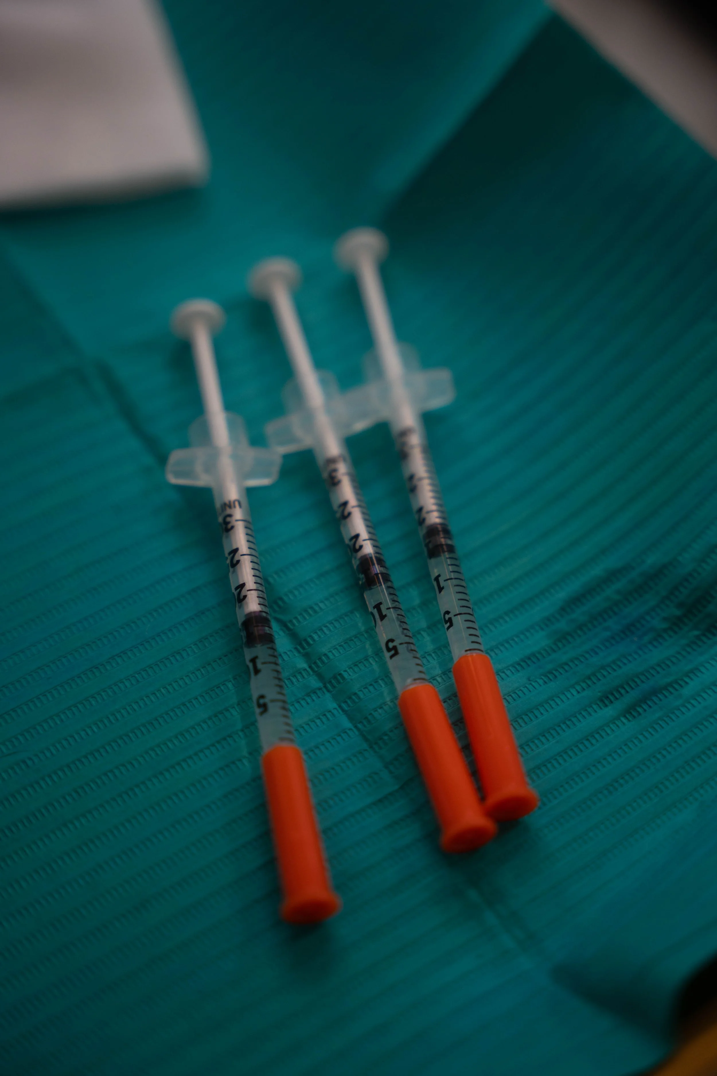 Three syringes with orange caps on a teal cloth surface