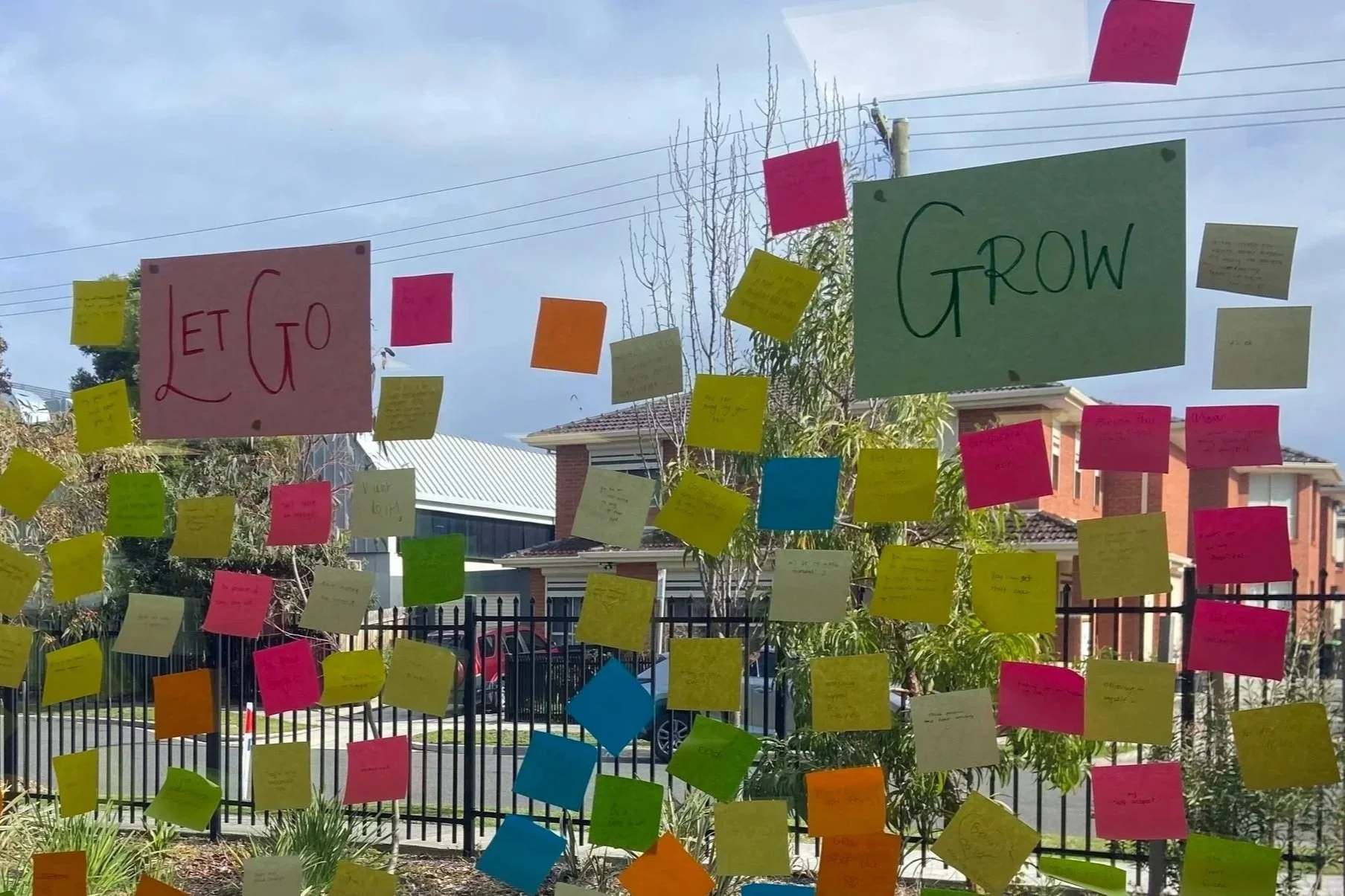 A window decorated with colourful sticky notes and signs that say "Let Go" and "Grow." Hand written messages of thoughts we want to develop and those we want to get rid of from our inner critics.