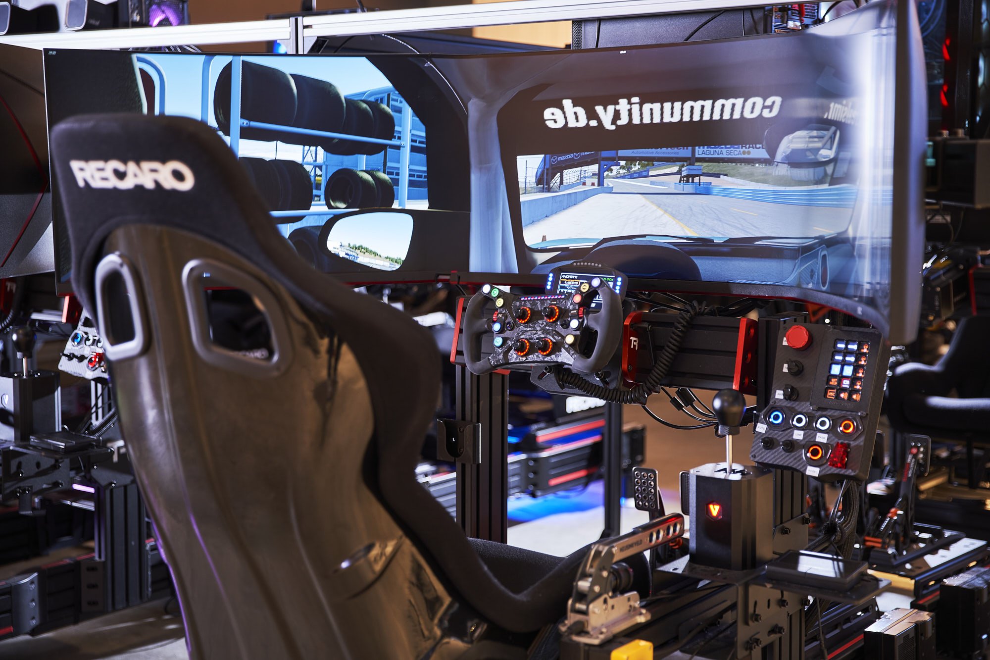 Person playing a racing simulator with a steering wheel and multiple monitors showing a racetrack.