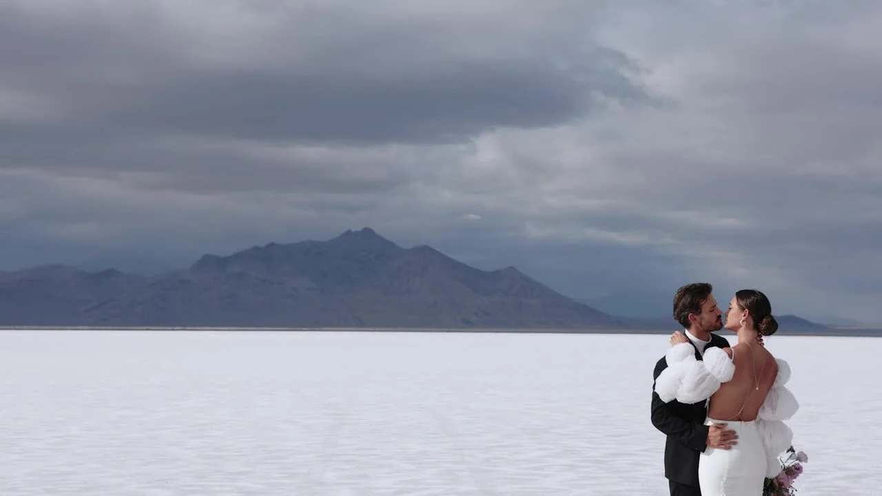 Wide embrace on the Bonneville Salt Flats, couple small against the white crust and storm clouds