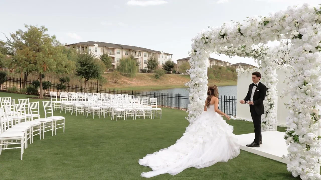 Bride in a ruffled white gown walking toward the groom under a white floral arch at Red Berry Estate