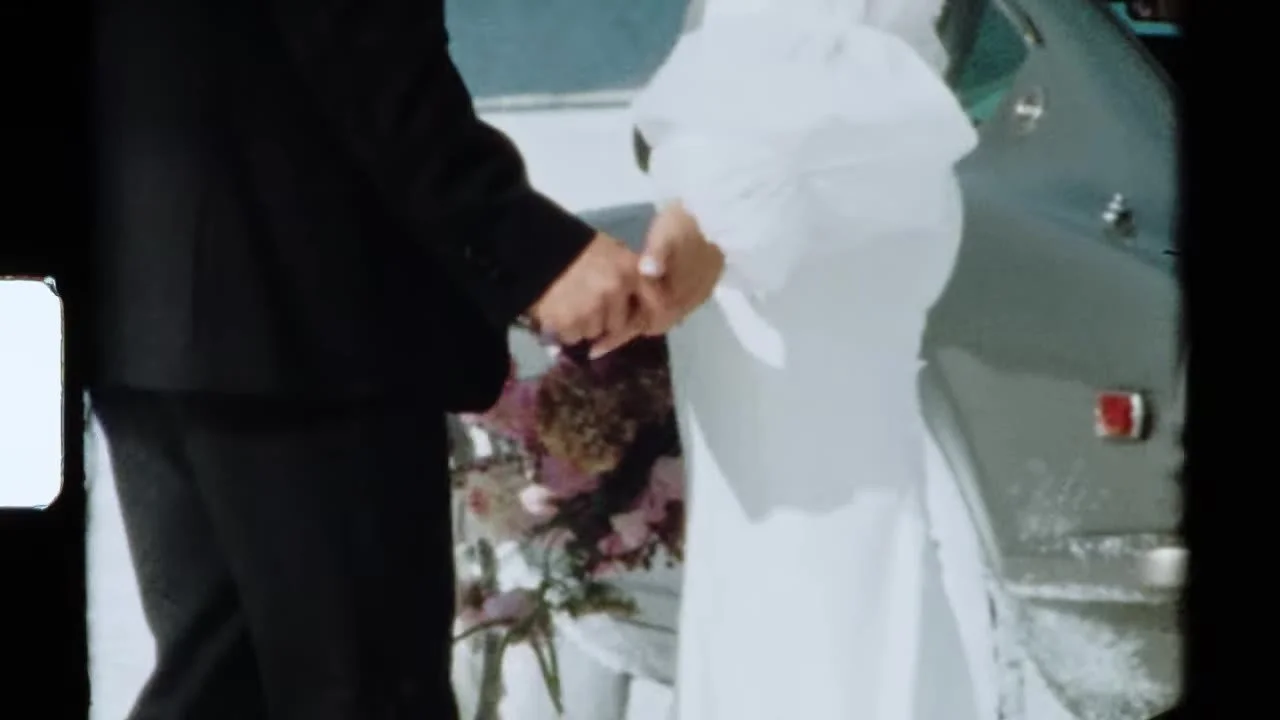 Super 8 tight shot of clasped hands at the 280Z quarter panel, pink bouquet and film grain
