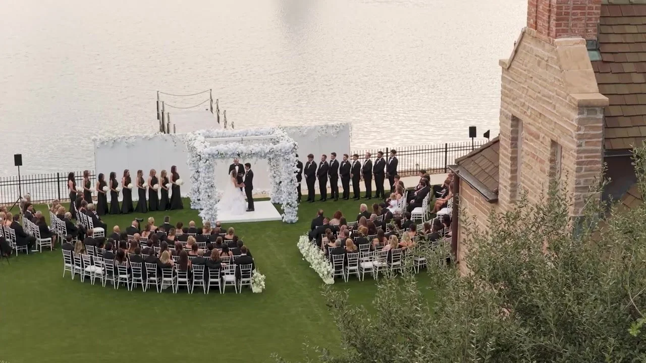 Corey and Emily under a white floral arch with their wedding party on the lawn at Red Berry Estate