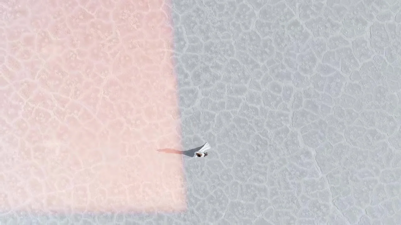 Aerial Super 8 still of a couple walking cracked Bonneville Salt Flats with pink light leak, by Austin videographer Adam Grumbo