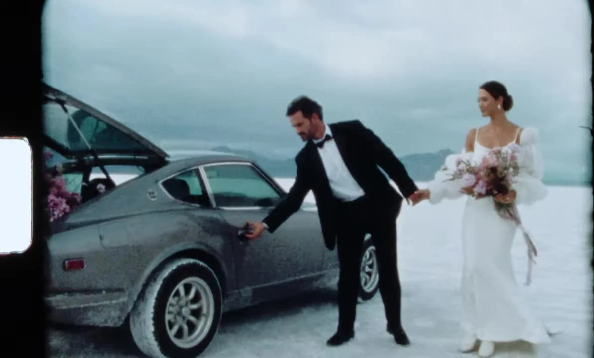 Super 8 frame of the couple at the open door of the 280Z, hatch filled with pink flowers