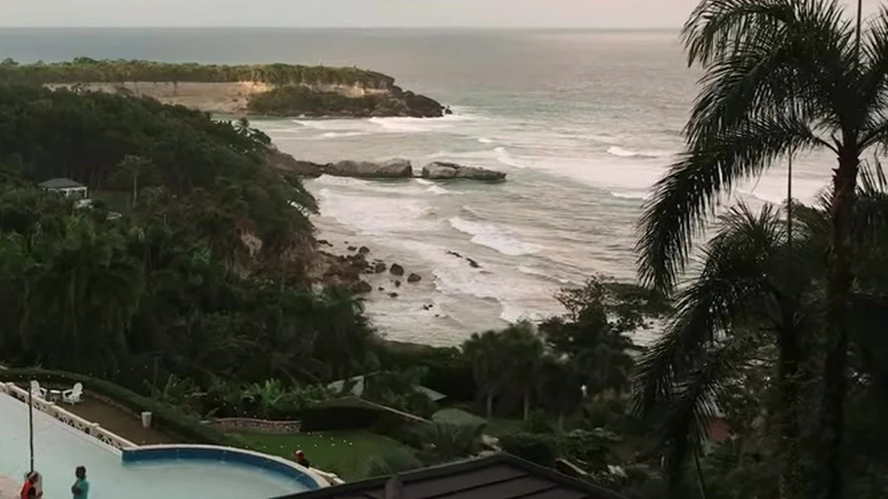 Palm, pool edge, and a forested headland over a sandy Dominican cove