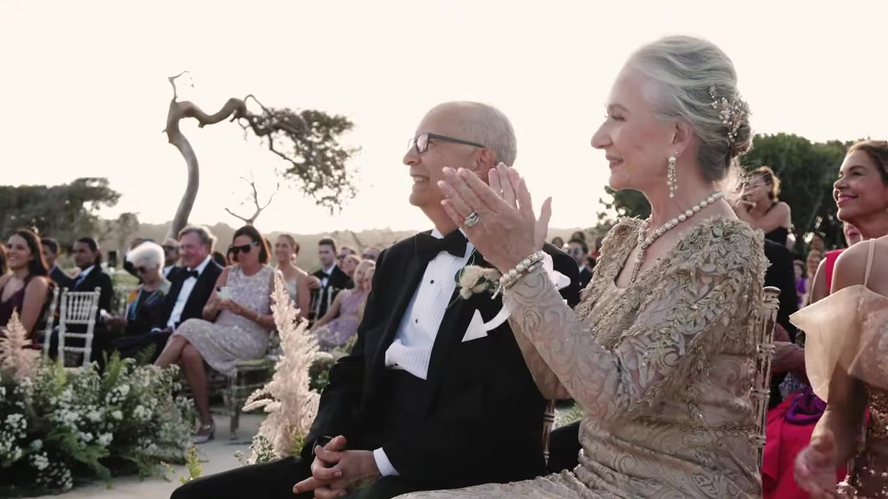 An older man in a tuxedo and a woman in gold lace clapping in the front row