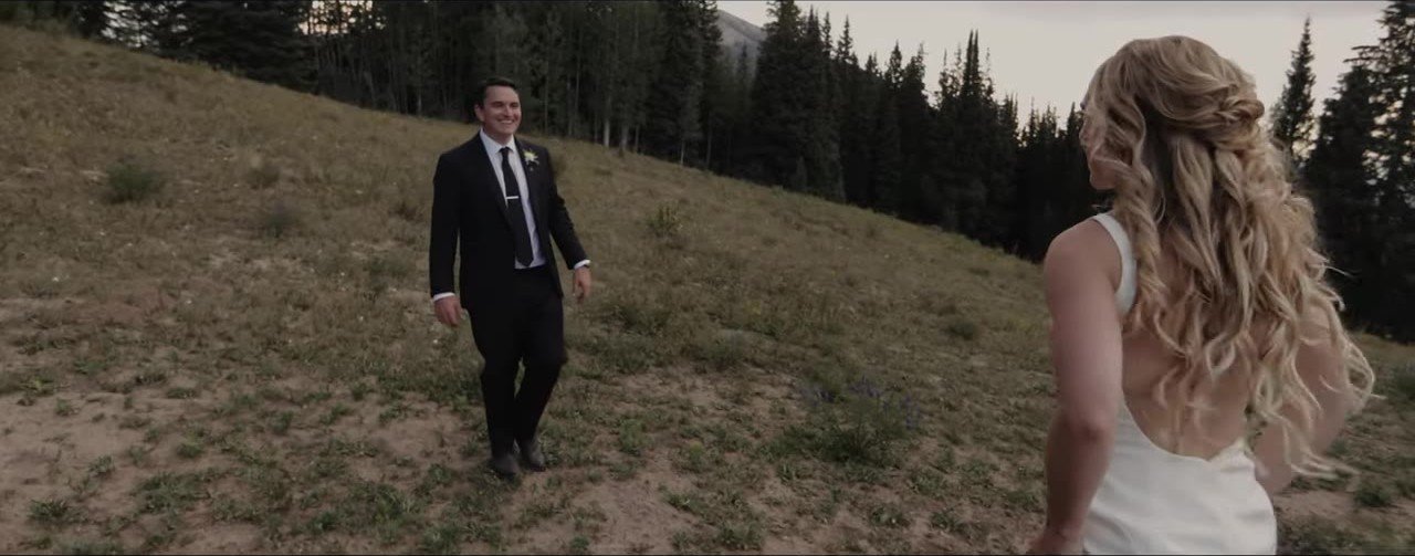 Davey walking toward Lauren on a grassy Crested Butte slope with evergreen forest behind them