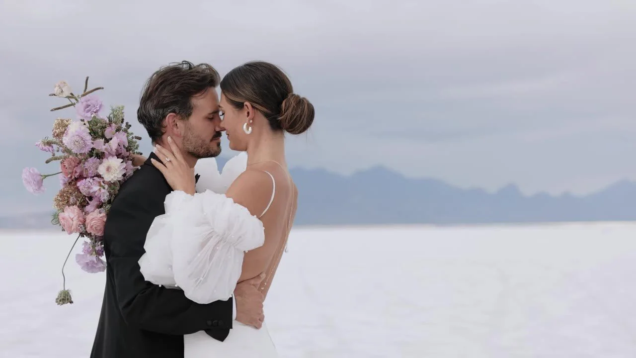 Tight embrace on the salt flats, noses together, puffy sleeves and a pink bouquet