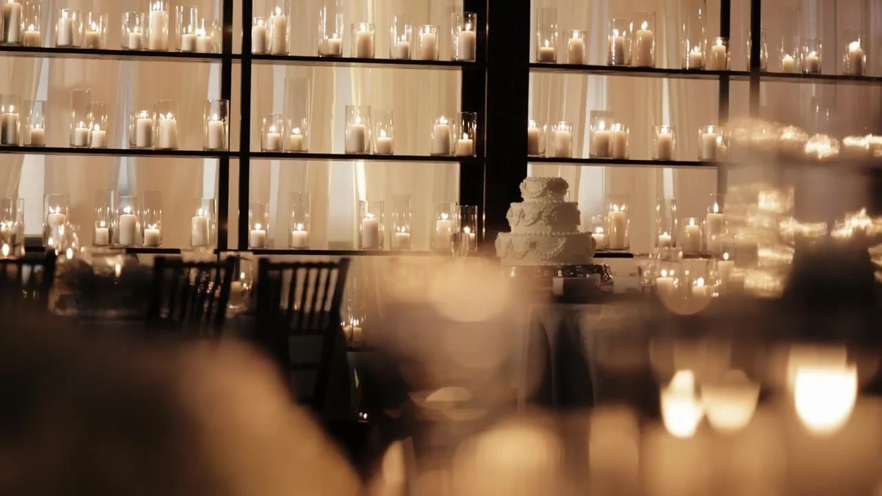 Three-tier white wedding cake in front of a wall of candles at a Red Berry Estate reception