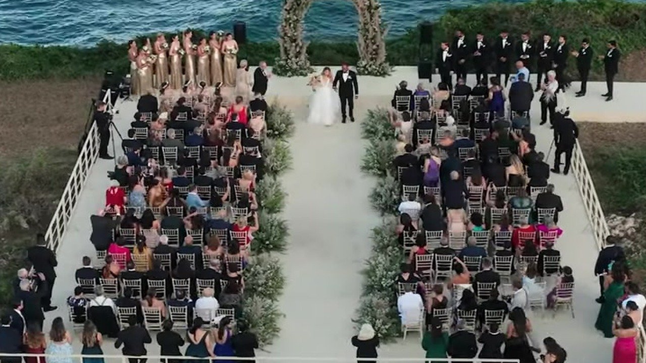 Felix and Victoria walking the pale aisle between gold chairs toward the circular cliff arch