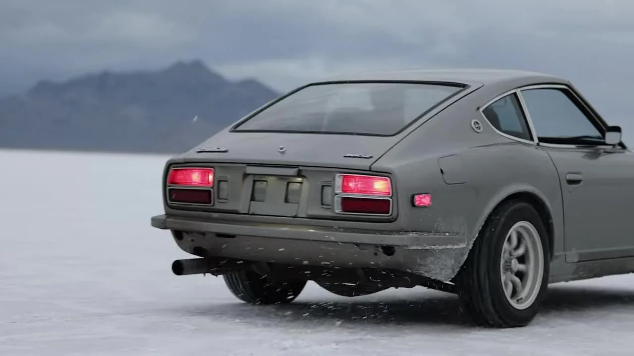 Vintage Datsun 280Z driving the Bonneville Salt Flats, salt spray off the tires, mountains ahead