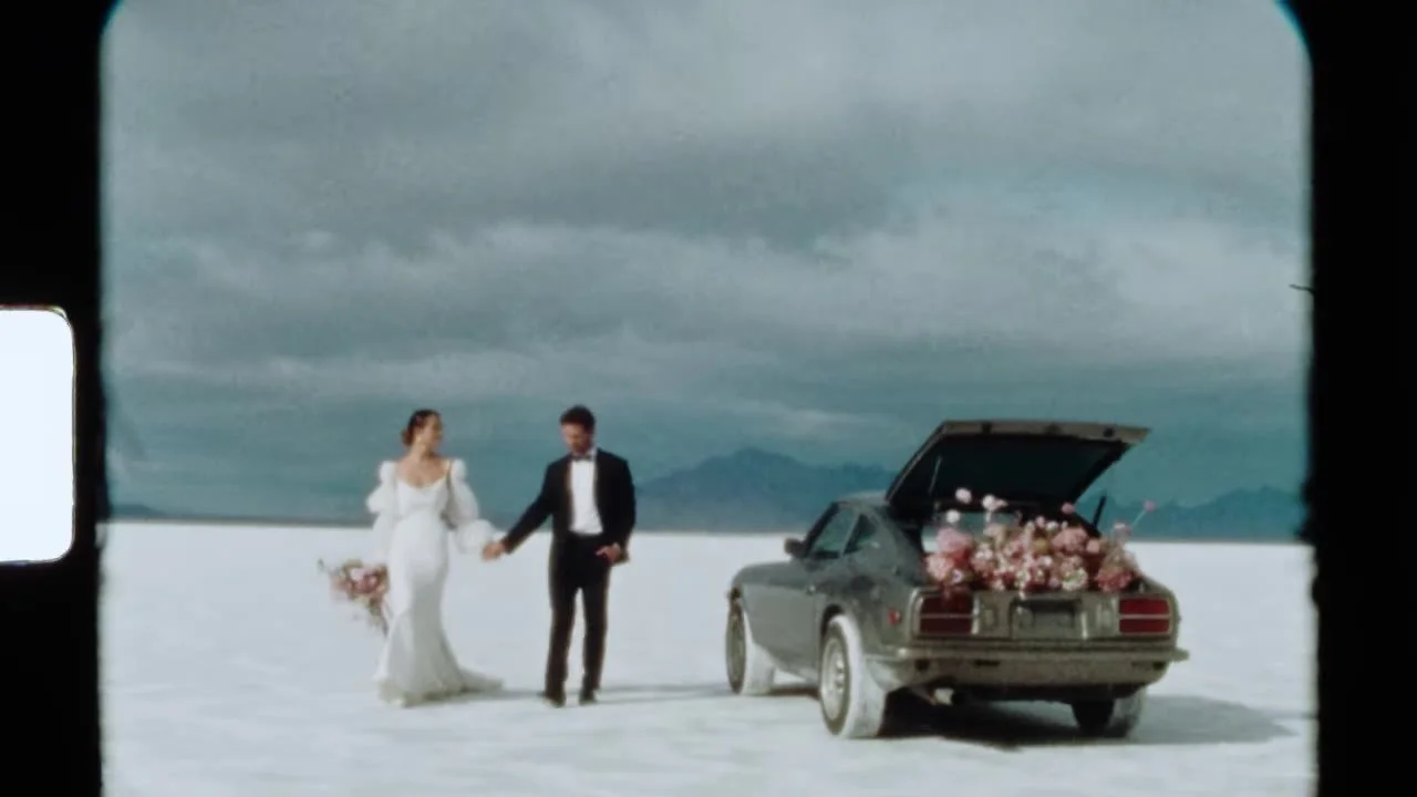 Super 8 frame of the couple walking toward the flower-filled 280Z on the salt flats, grain and sprocket flare