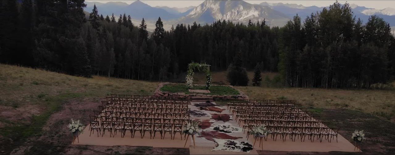 Empty Crested Butte ceremony site, wooden chairs and a floral arch facing forest and mountains