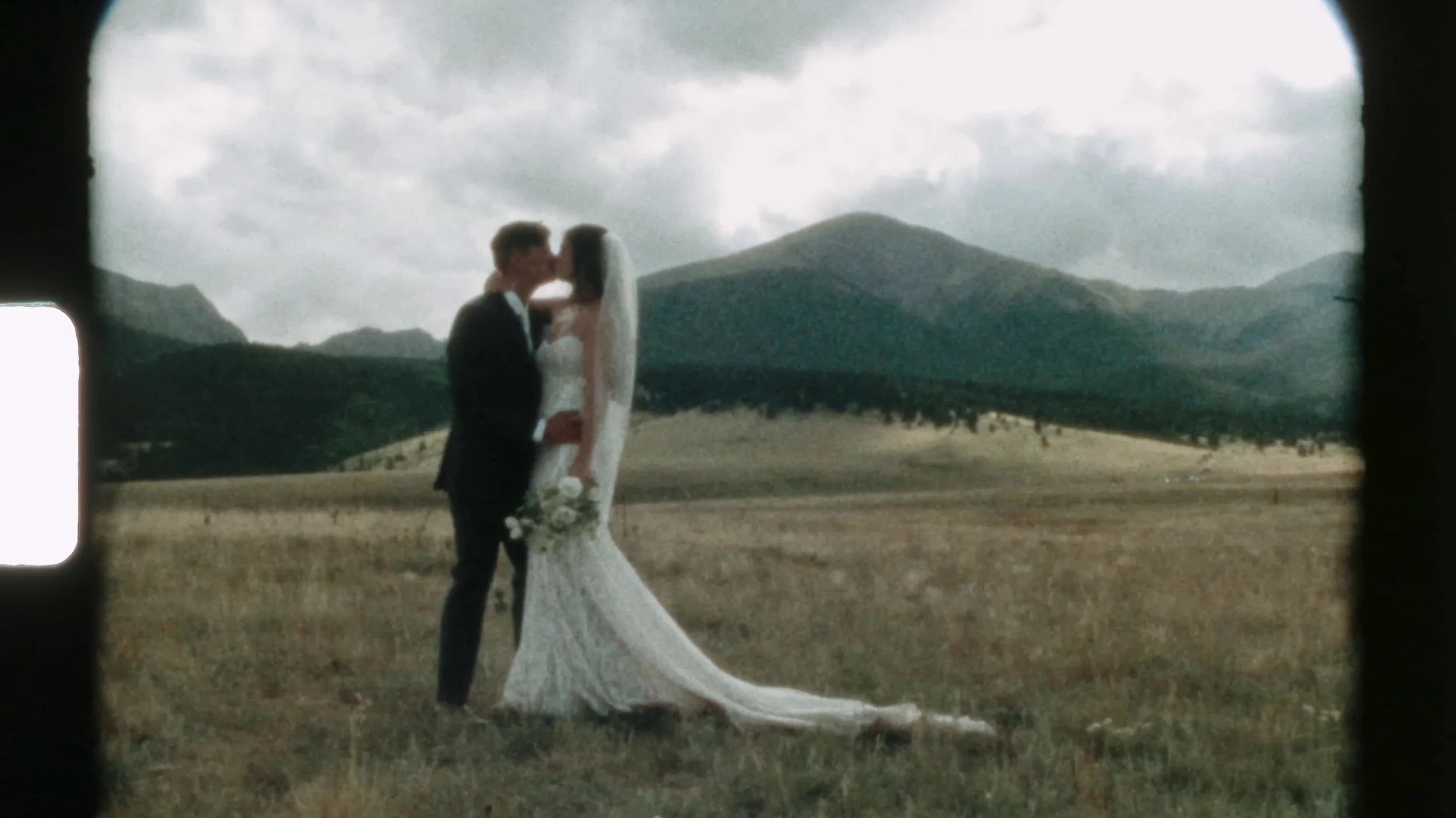 Super 8 frame of a kiss in a meadow at 3 Peaks Ranch with Colorado mountains, film grain and sprocket flare
