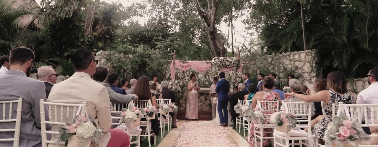Wide ceremony at Mahekal: royal blue suit, rose-gold officiant, pink petal aisle