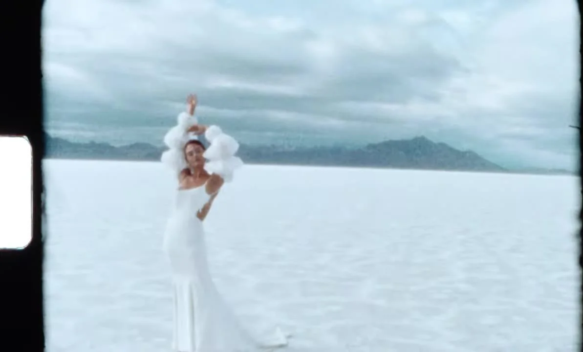 Super 8 frame of the bride standing alone on the salt flats with arms raised, film grain and sprocket flare