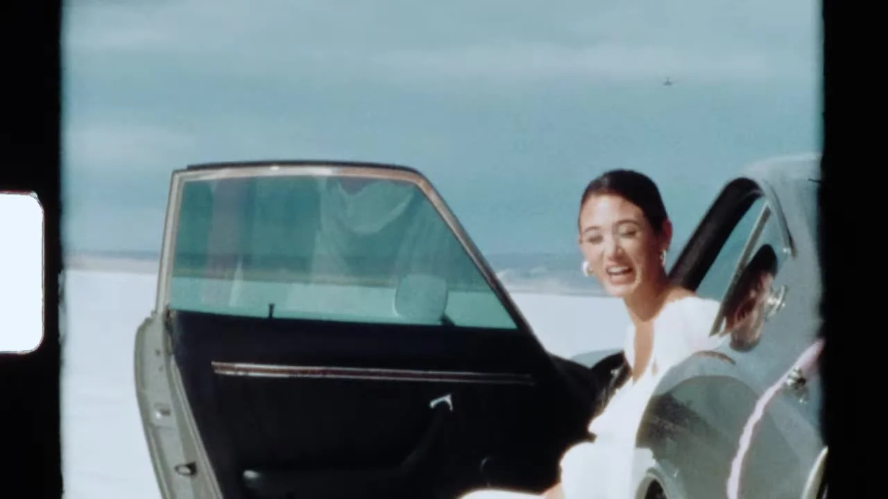 Super 8 frame of the bride laughing in the open door of the 280Z on the salt flats, grain and sprocket edge