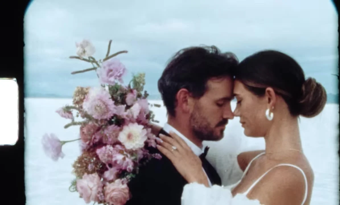 Super 8 tight shot of the couple forehead to forehead, bouquet in pink and lavender, salt horizon behind them