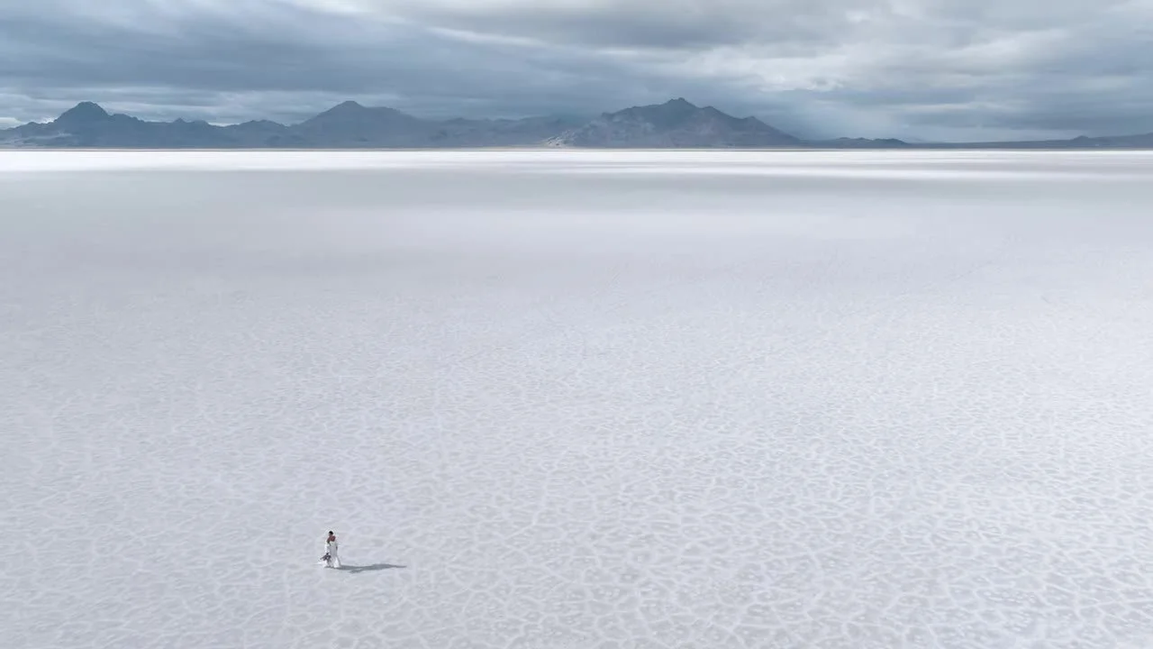 Extreme wide aerial of the couple small on the cracked white salt with mountains on the horizon