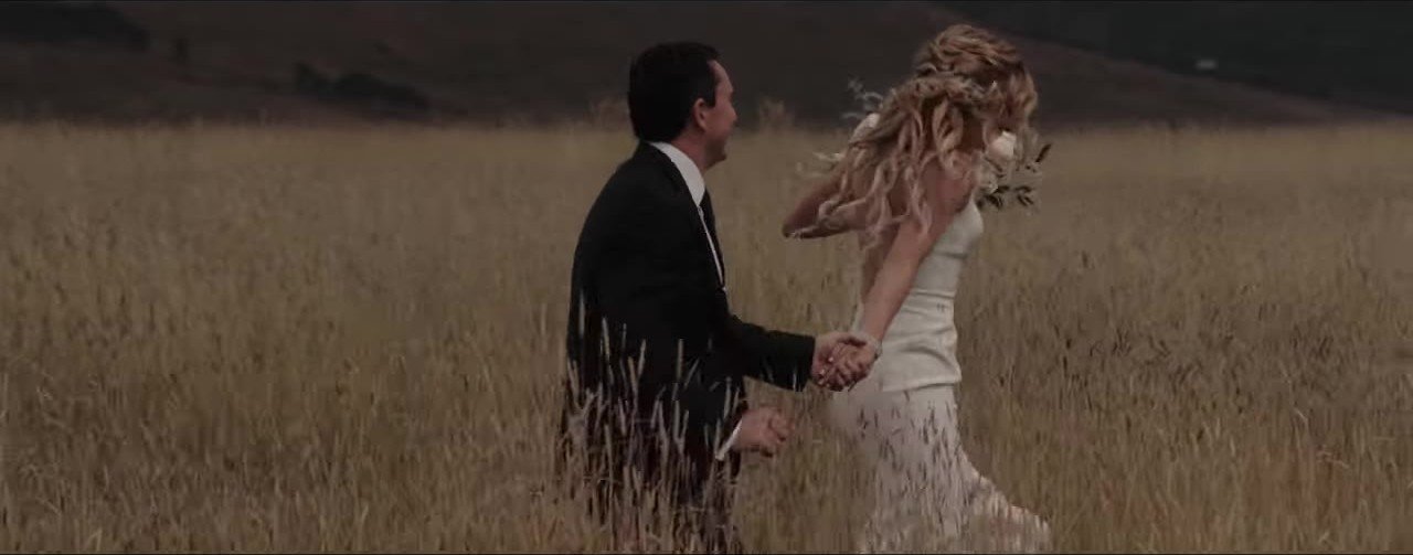 Lauren and Davey running hand in hand through tall golden grass in Crested Butte