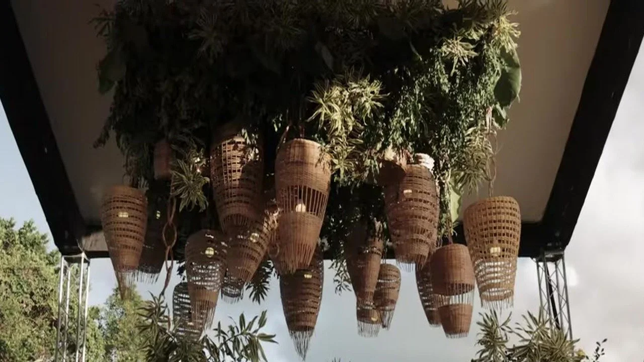 Looking up at woven wicker lanterns hanging from a dense greenery canopy