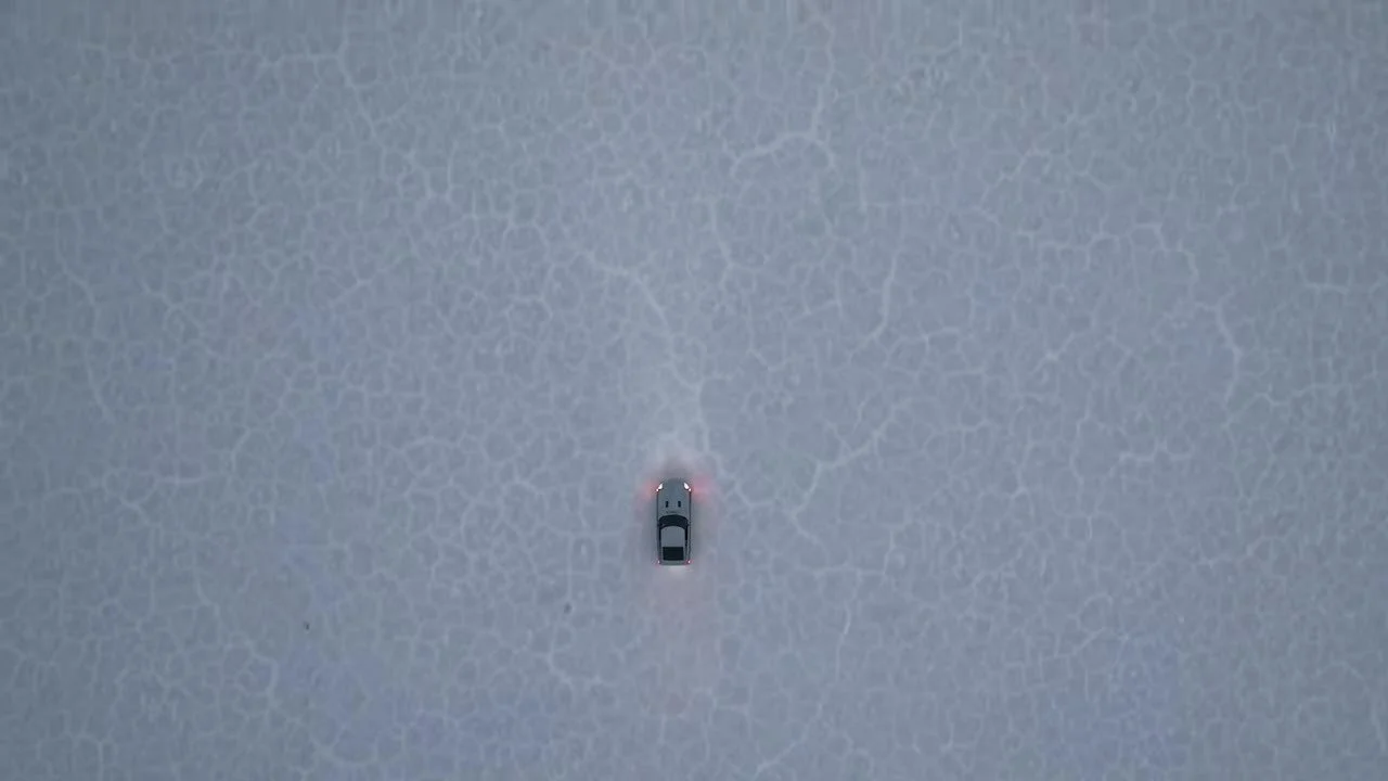 Top-down drone of the vintage 280Z parked on cracked white salt, taillights on, environment filling the frame