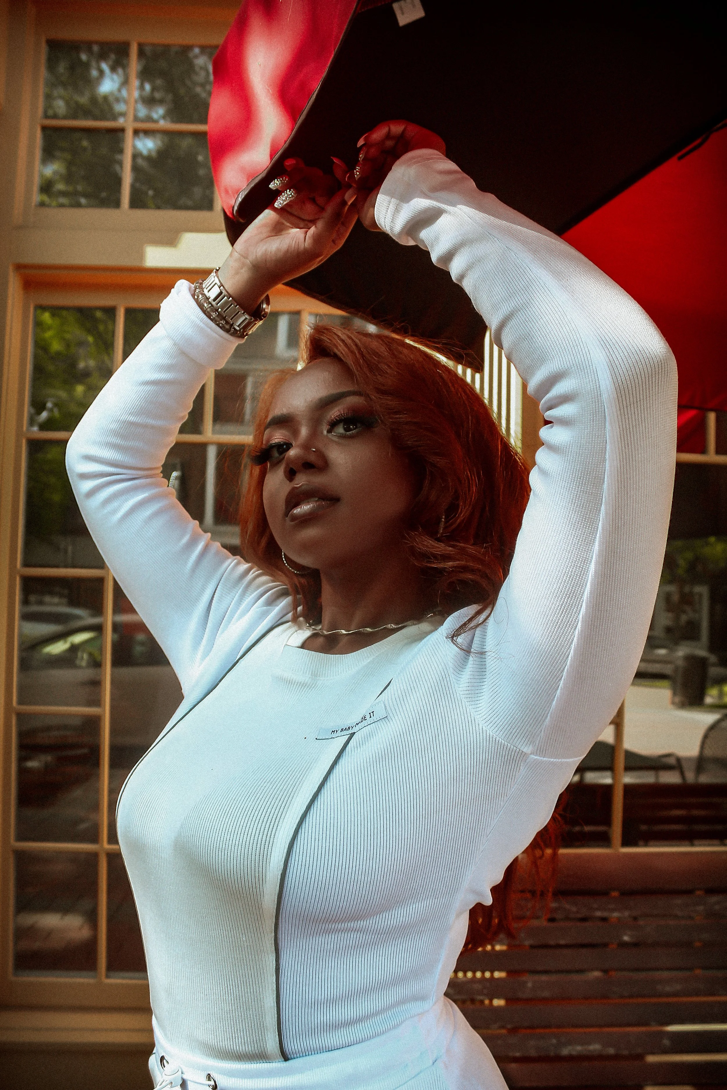 Person in white outfit posing under red umbrella