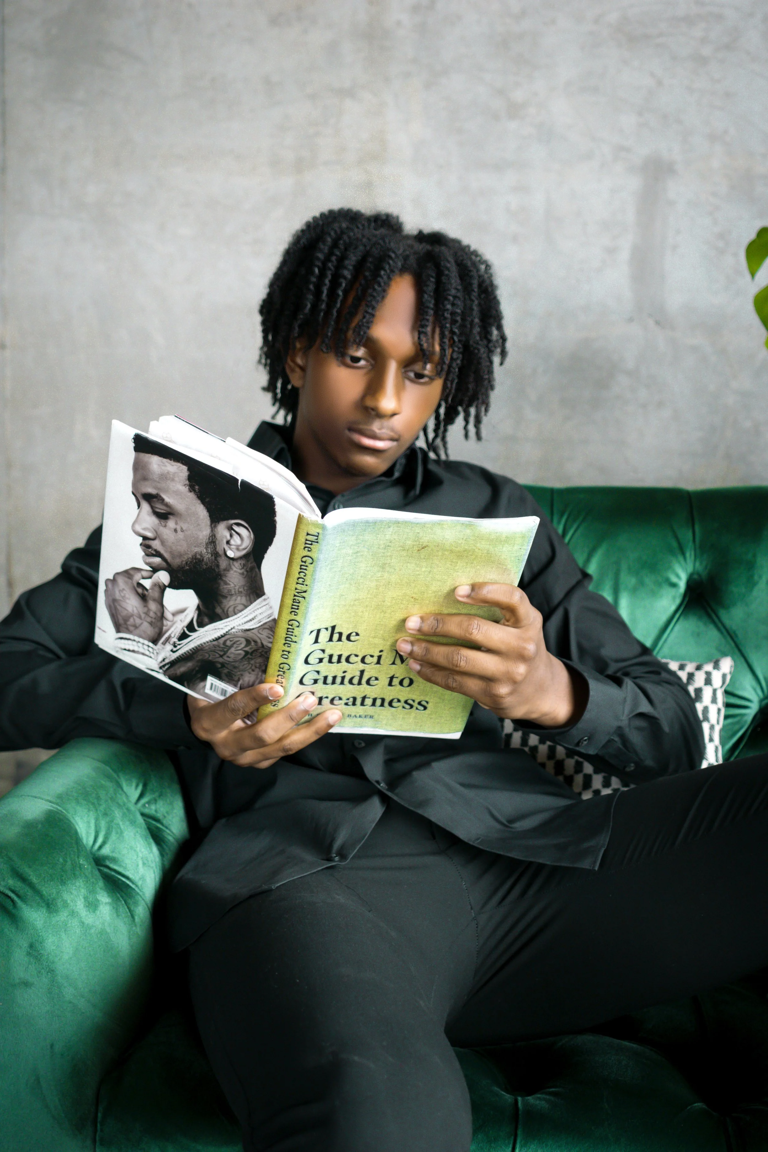 Person reading 'The Gucci Mane Guide to Greatness' on a green sofa.