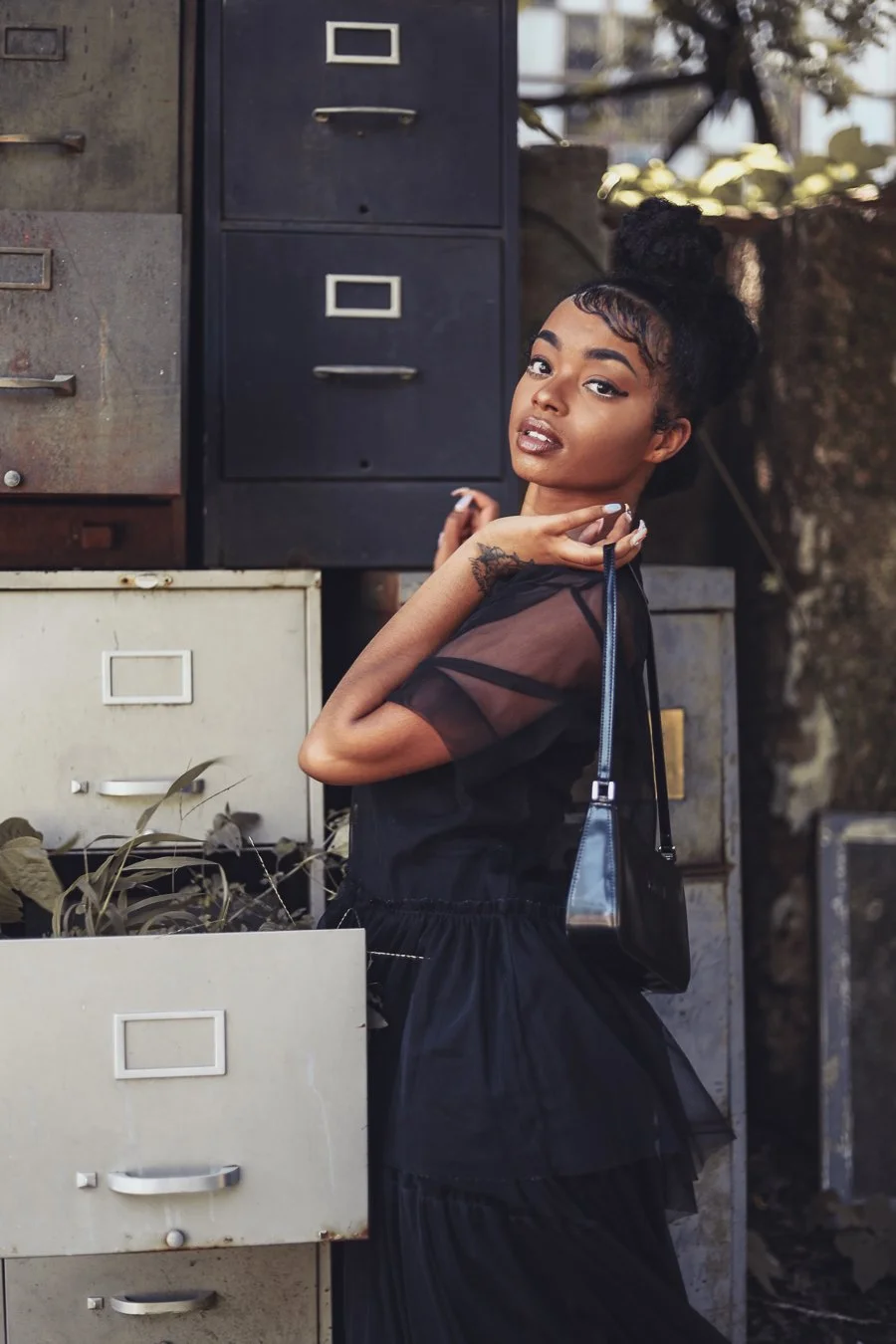 Woman in black dress posing outdoors with vintage file cabinets.