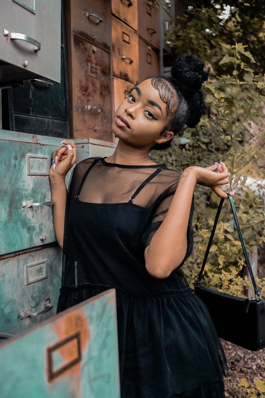 Woman in black dress posing near vintage file cabinets outdoors.