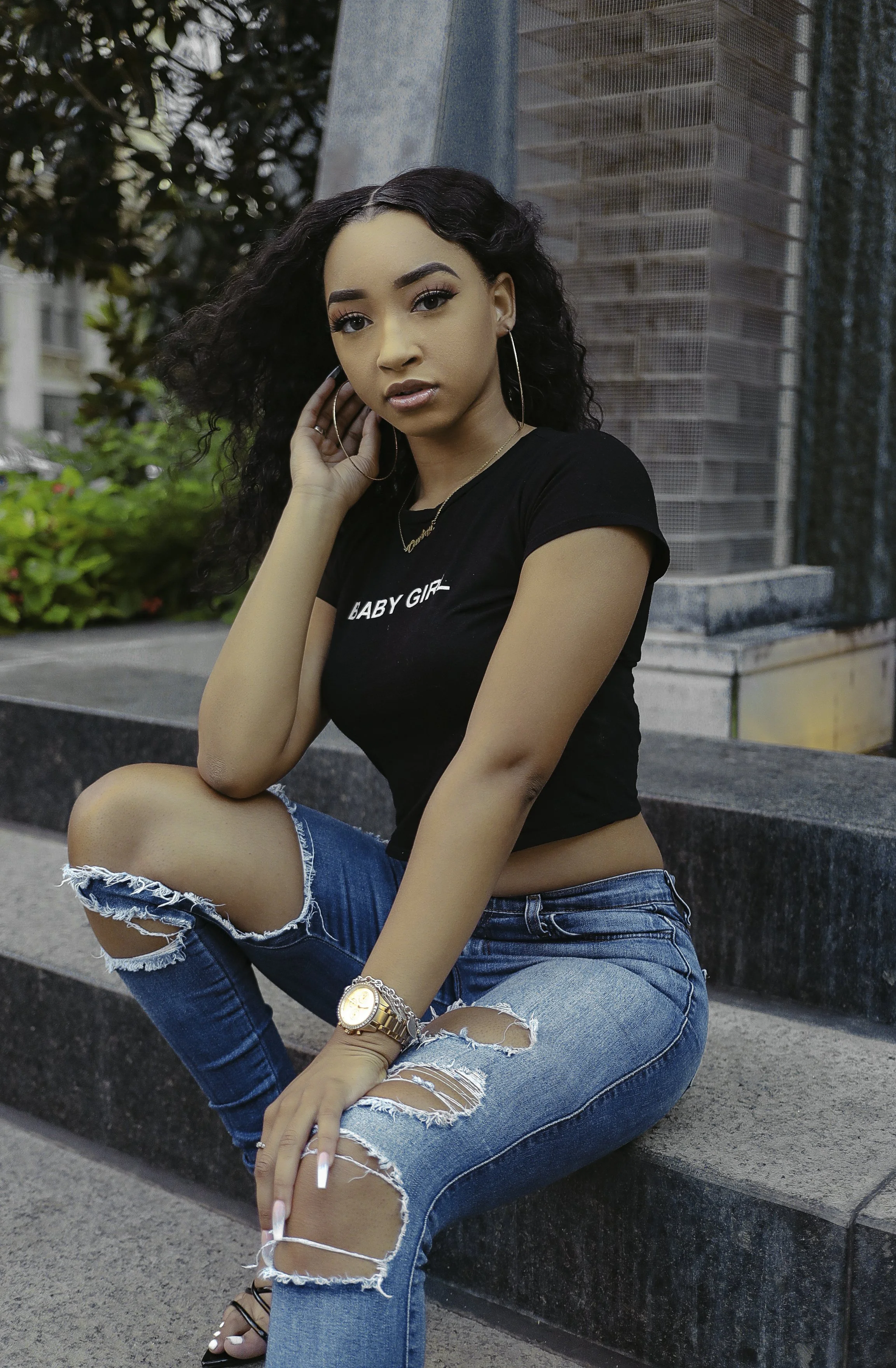 Woman with curly hair sitting on steps, wearing ripped jeans and a black t-shirt.