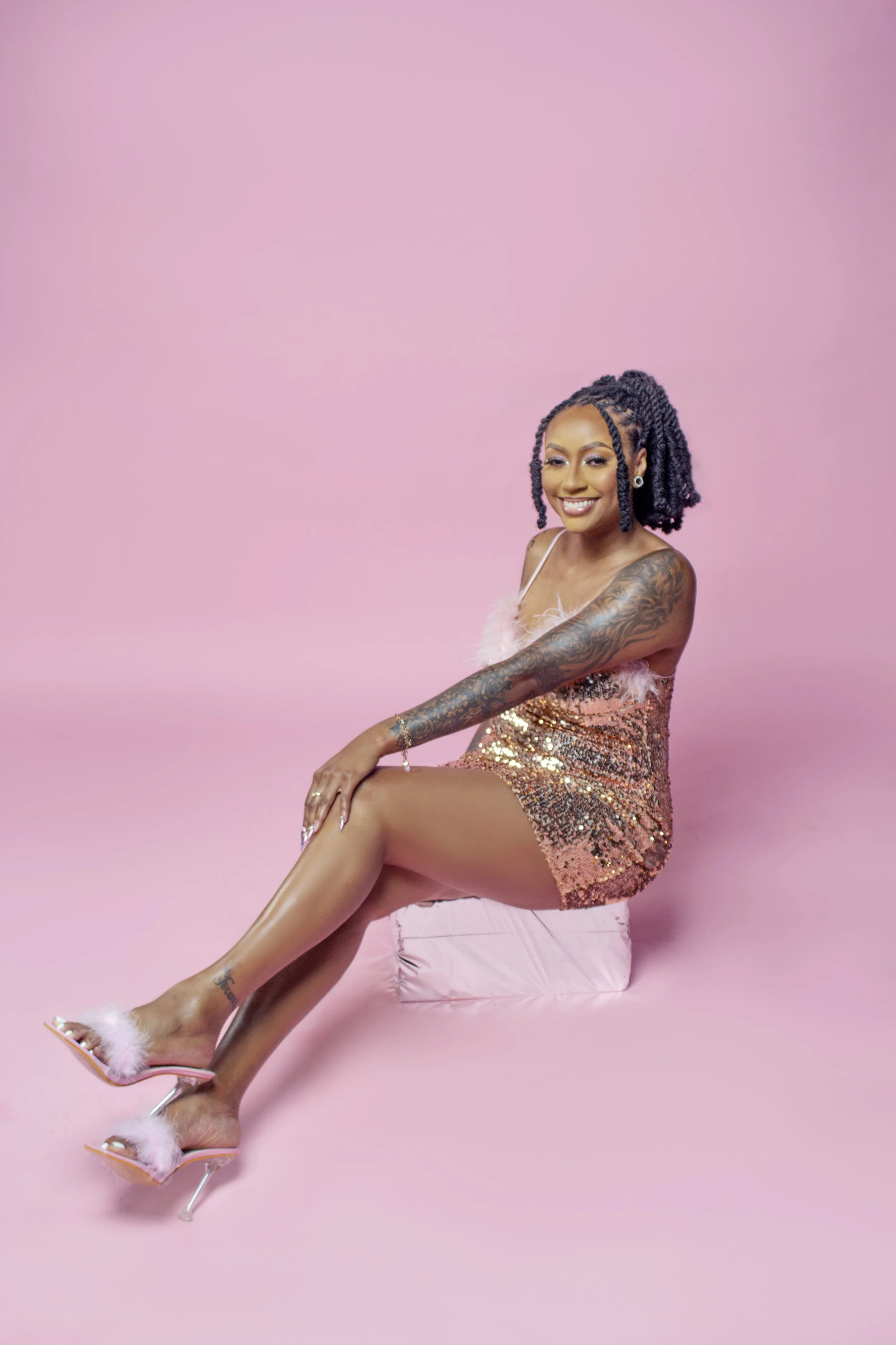 Smiling woman in sequin dress sitting on pink background