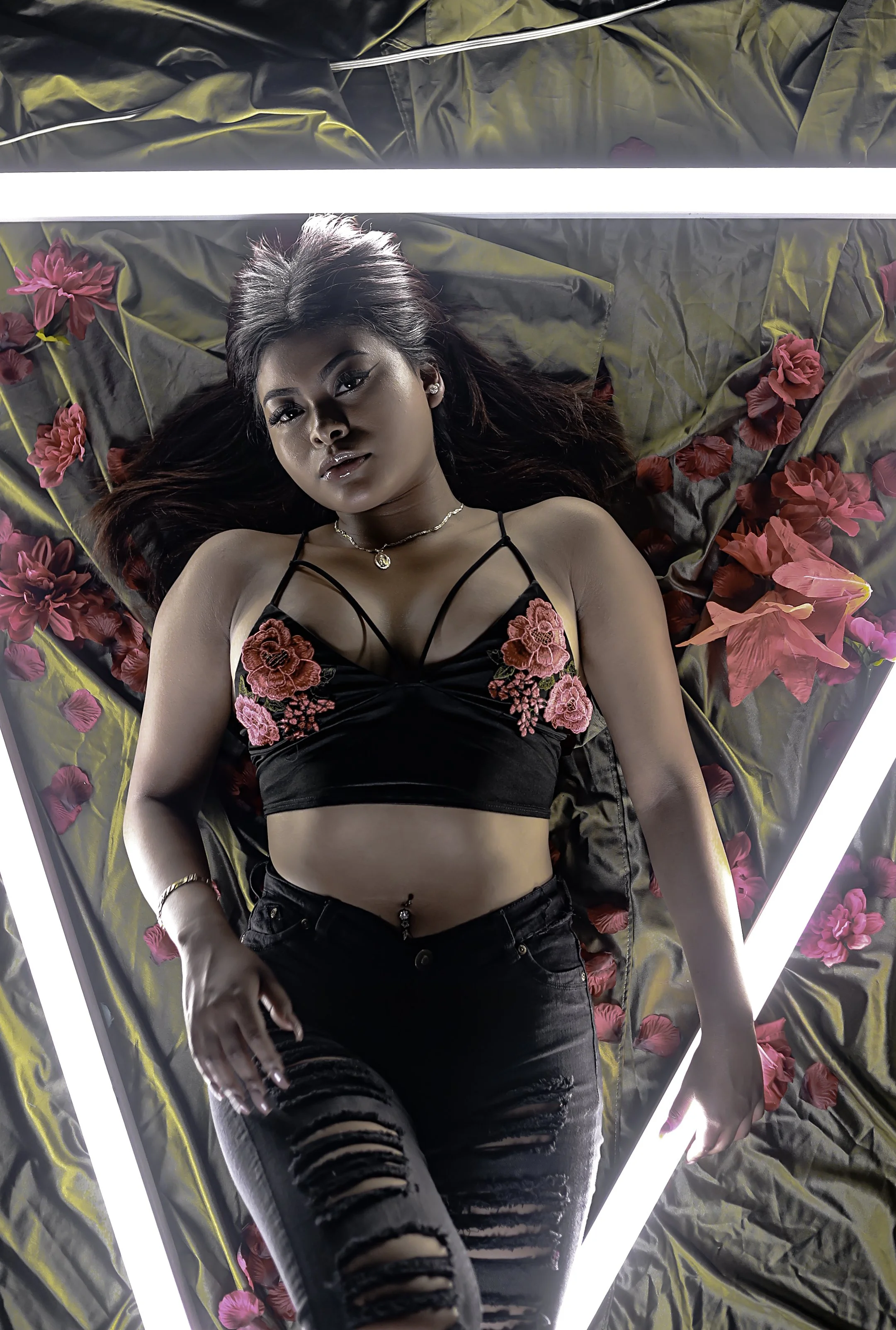 Woman lying on black and red floral sheet surrounded by LED strip lights