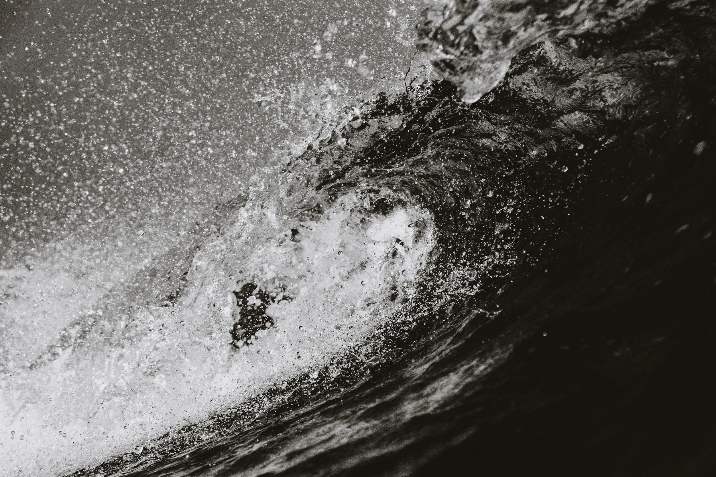 Black and white photograph of a breaking ocean wave with water droplets.