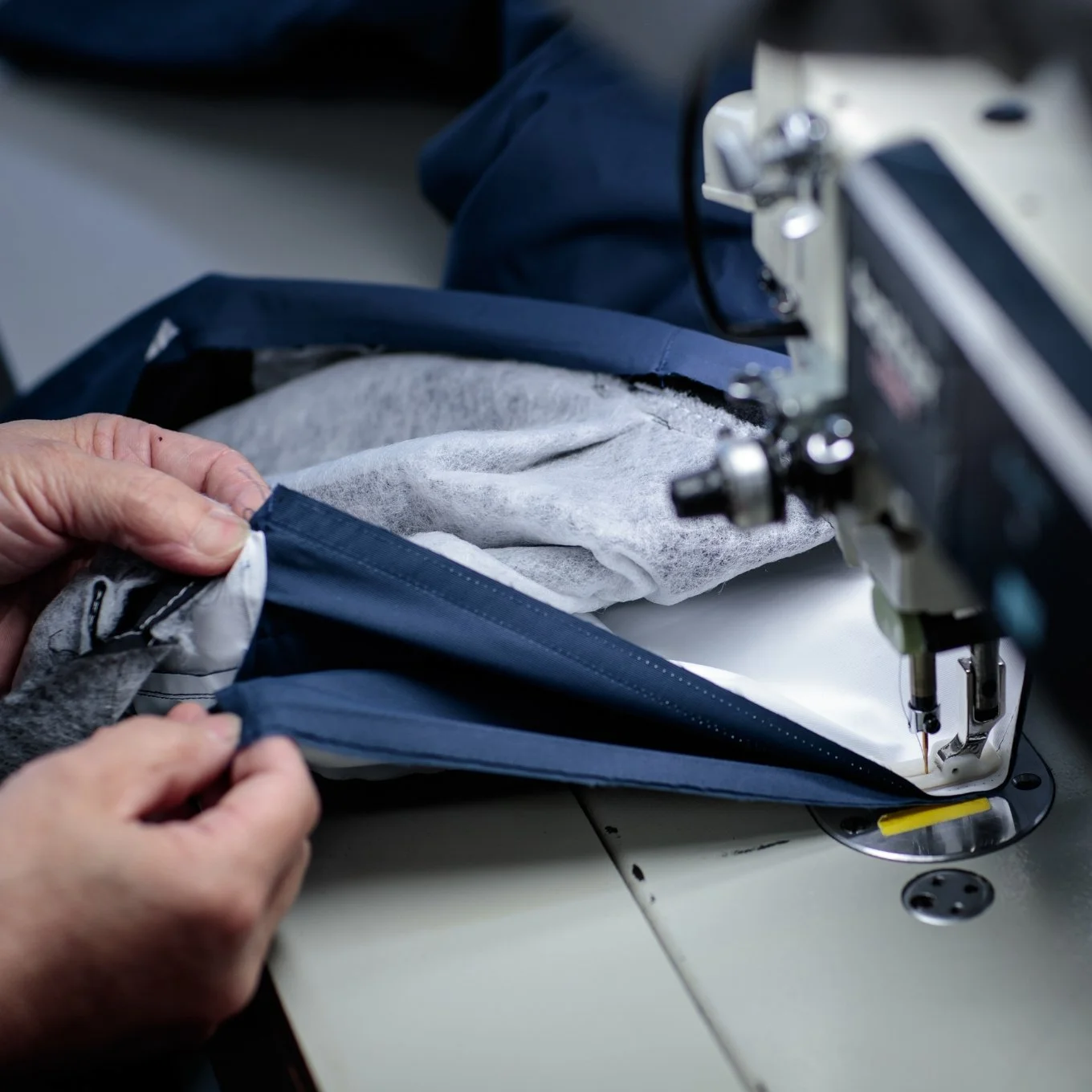 Person sewing dark blue fabric with industrial sewing machine.