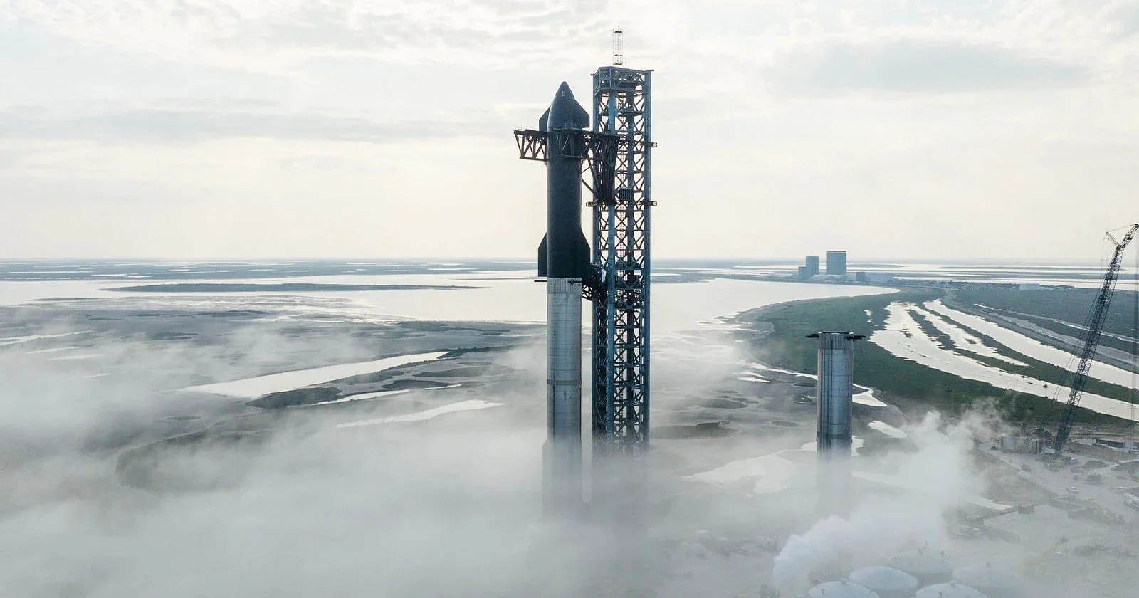 A SpaceX Falcon rocket on a launch pad with fog and water bodies in the background.