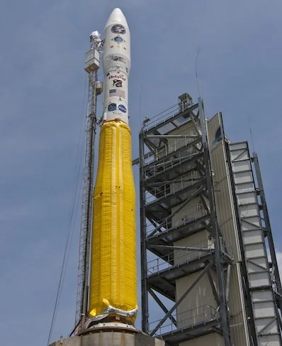 A space rocket on a launch pad with a tall structure and stairs beside it, against a cloudy sky.