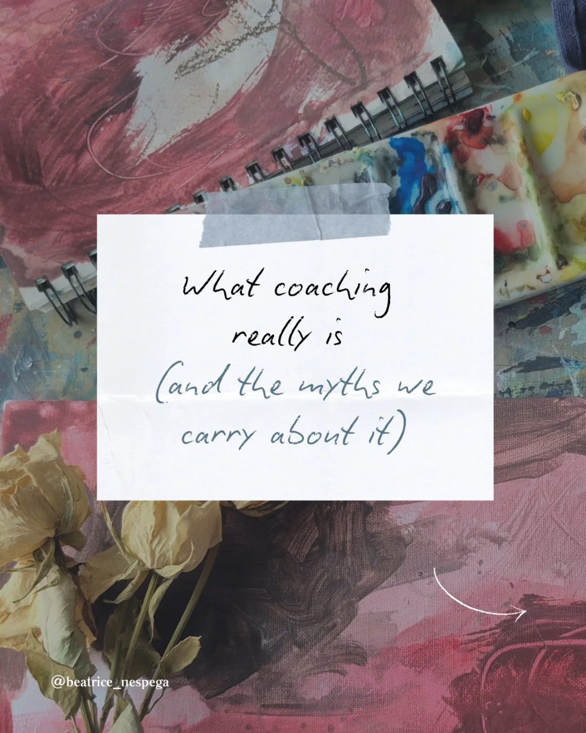 A white note with handwritten text that says, "What coaching really is (and the myths we carry about it)," taped onto a colorful, abstract art background. The background features a spiral-bound sketchbook with an pink and brown abstract painting, some paint palette swatches, and dried white flowers in the foreground.
