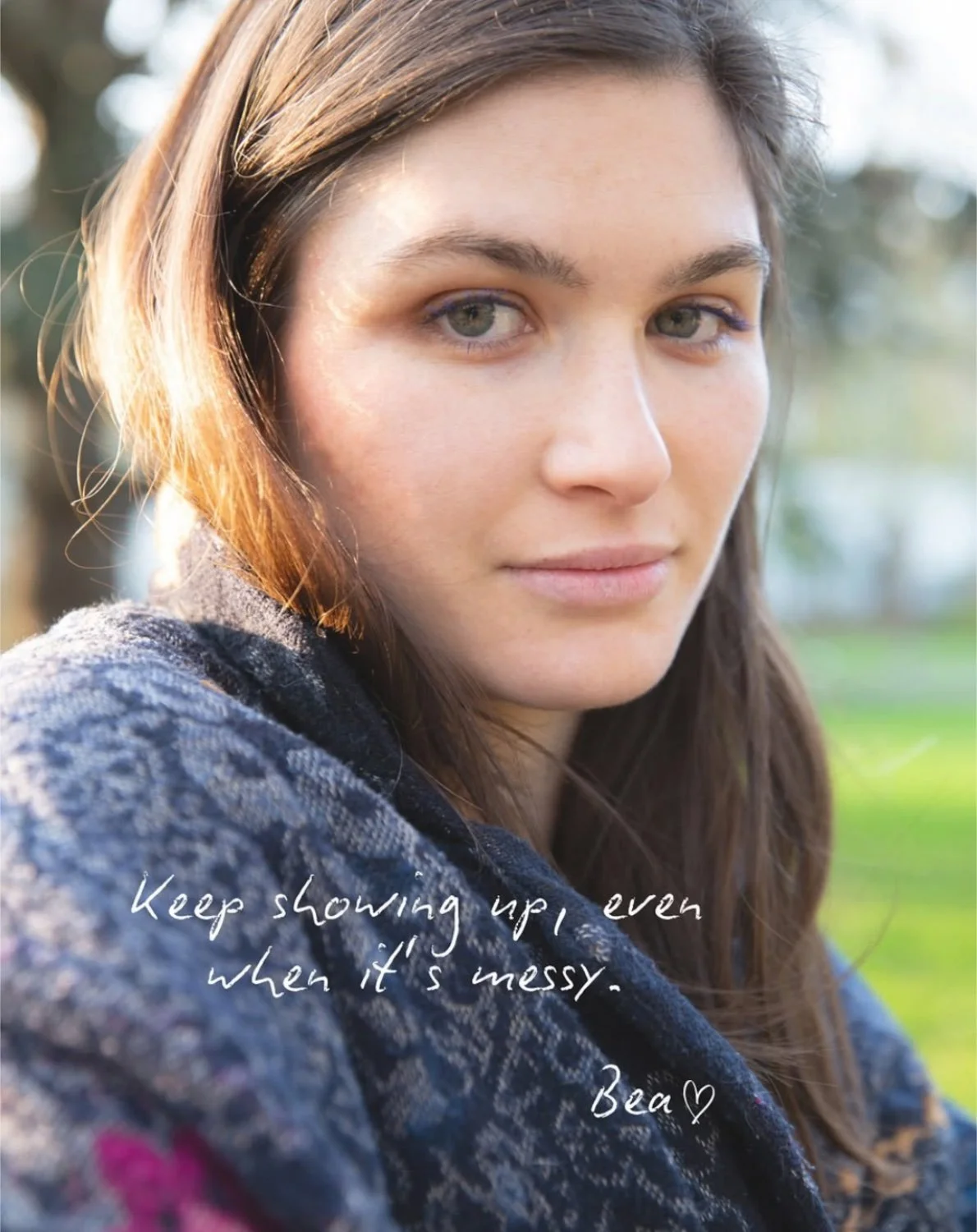 A close-up photo of a young woman with light brown hair and green eyes, outdoors with trees and grass in the background, wearing a patterned dark jacket. Overlaid text reads, 'Keep showing up, even when it's messy. Bea ♥'