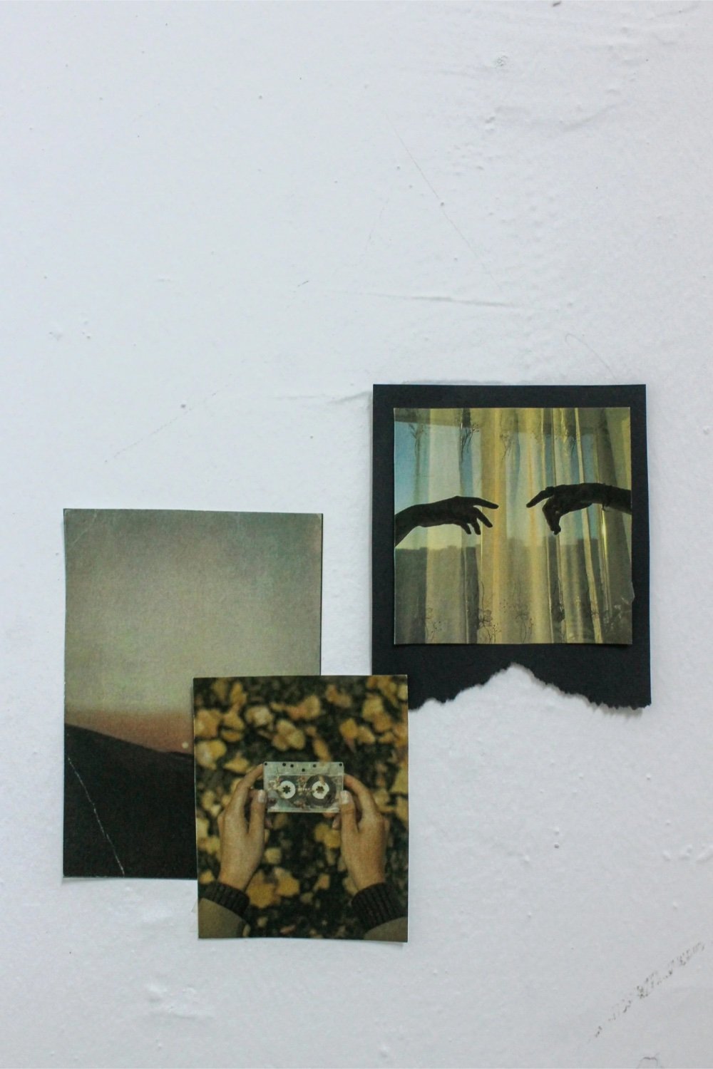 Three photographs on a white wall: a landscape with a mountain, a close-up of hands holding a cassette tape, and a framed picture of two hands reaching towards each other.