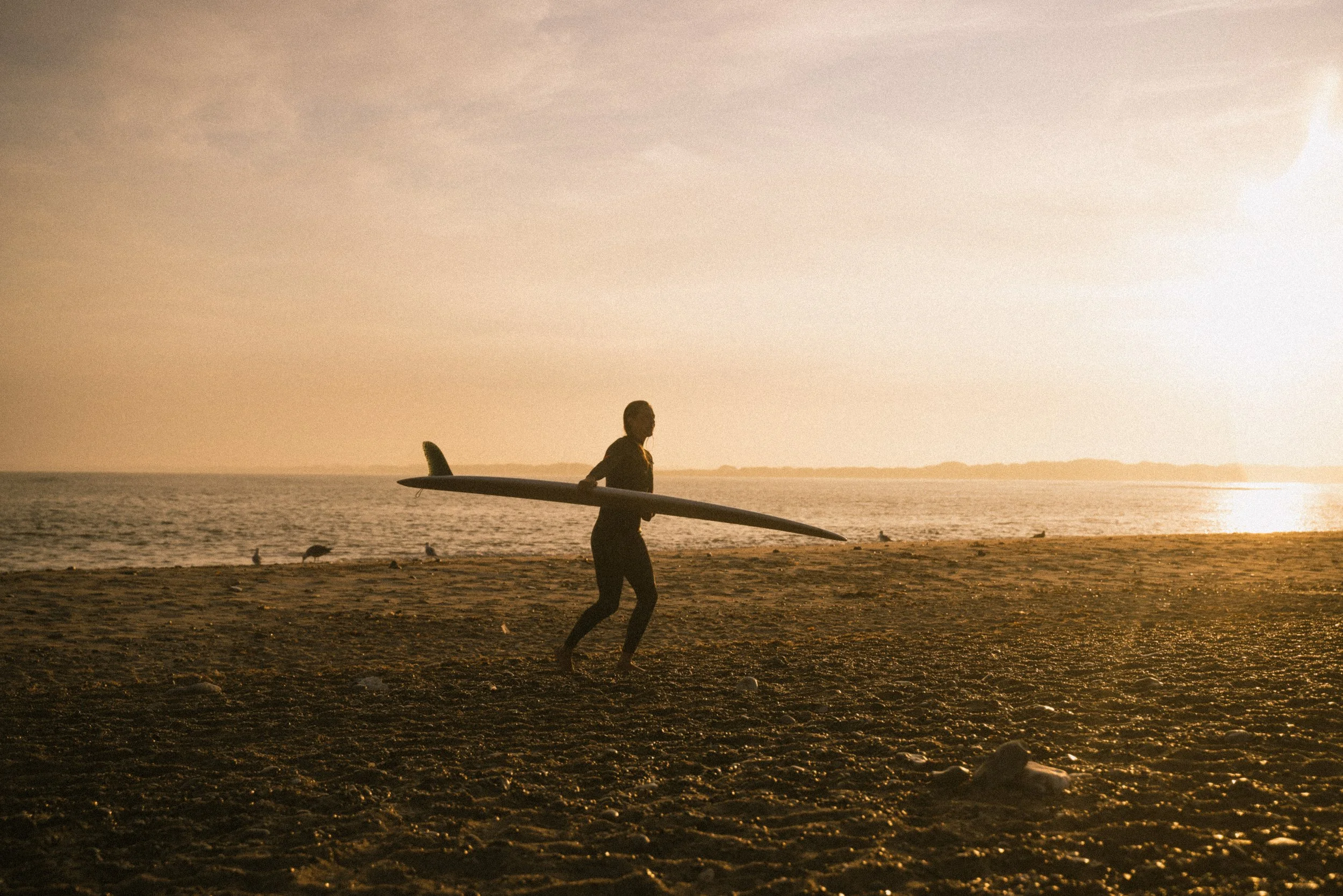 Ein Mensch läuft am Strand mit einem Surfbrett bei Sonnenuntergang.