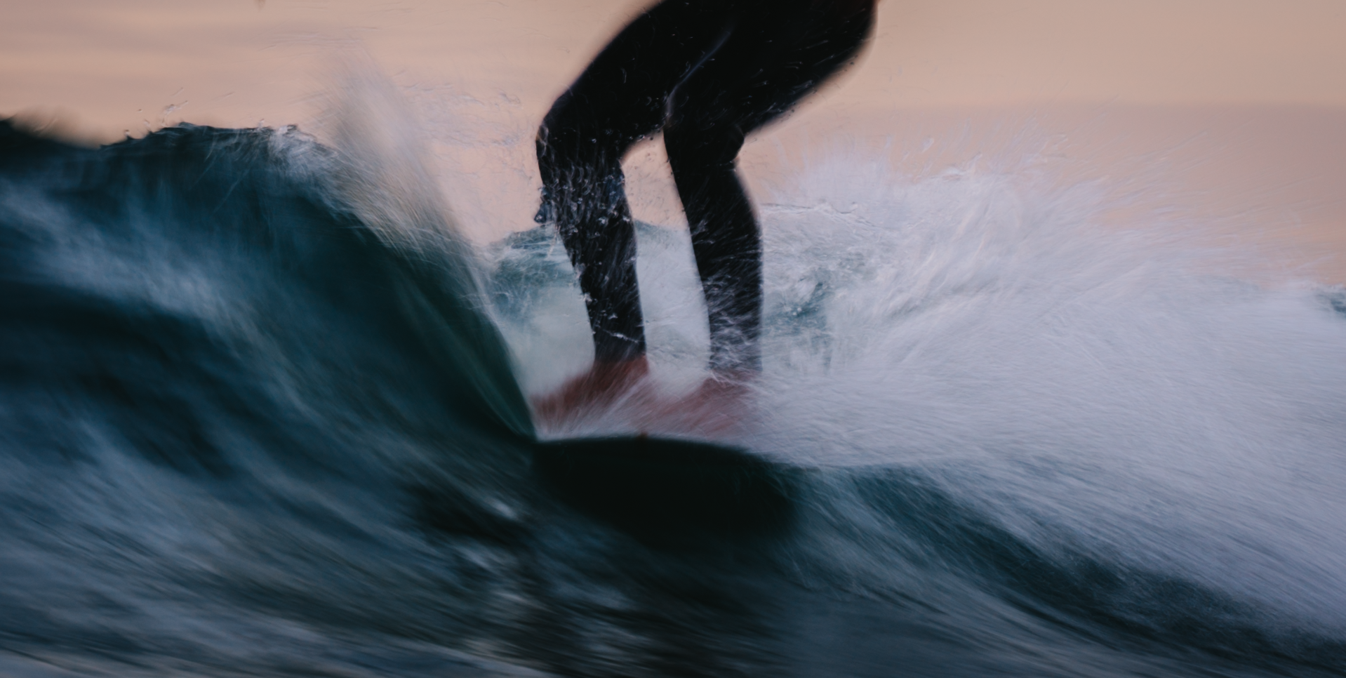 Segler auf einem Surfboard reitet eine Welle bei Sonnenuntergang.
