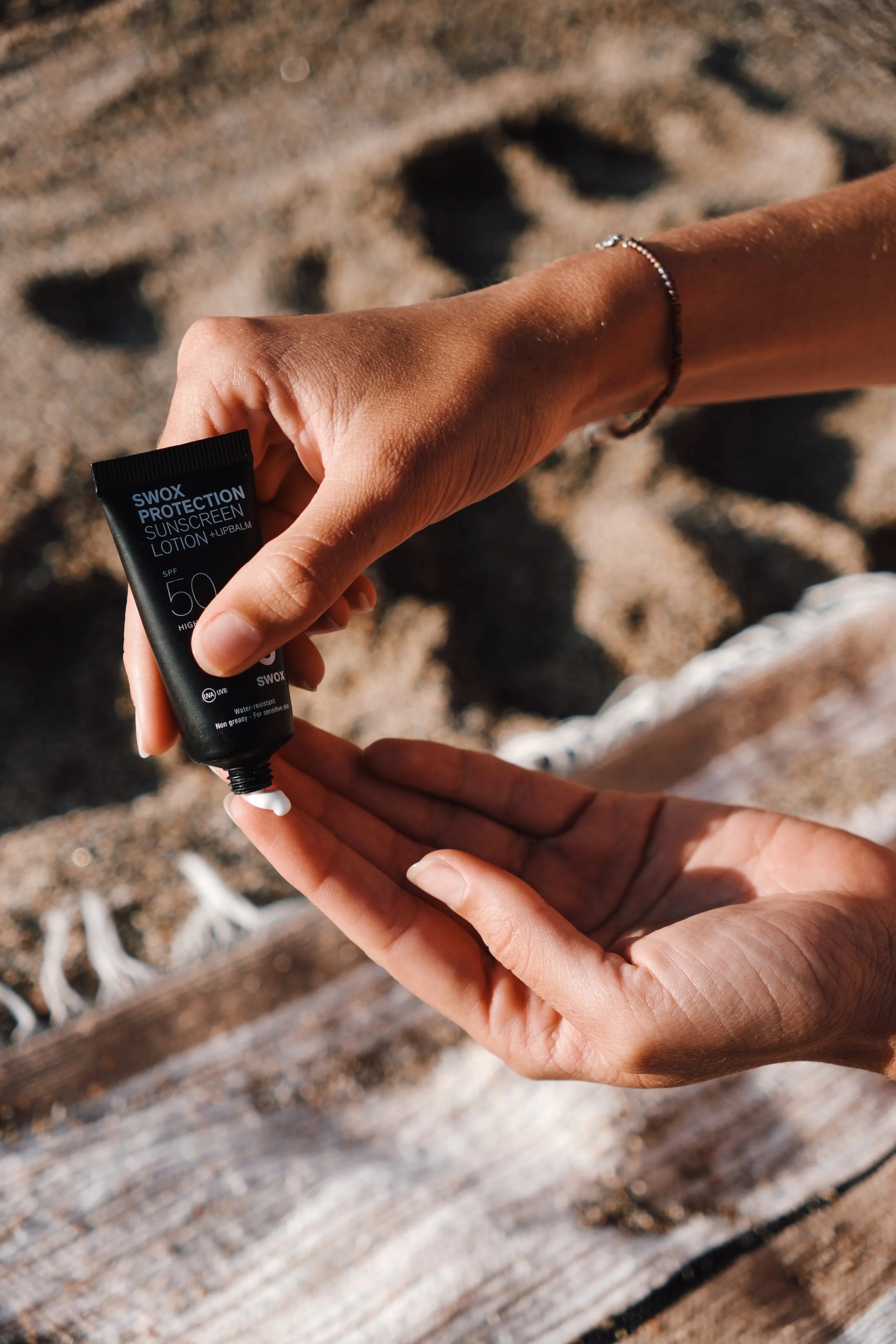Person trägt Sonnencreme auf die Hand auf am Strand mit Sand und Holz