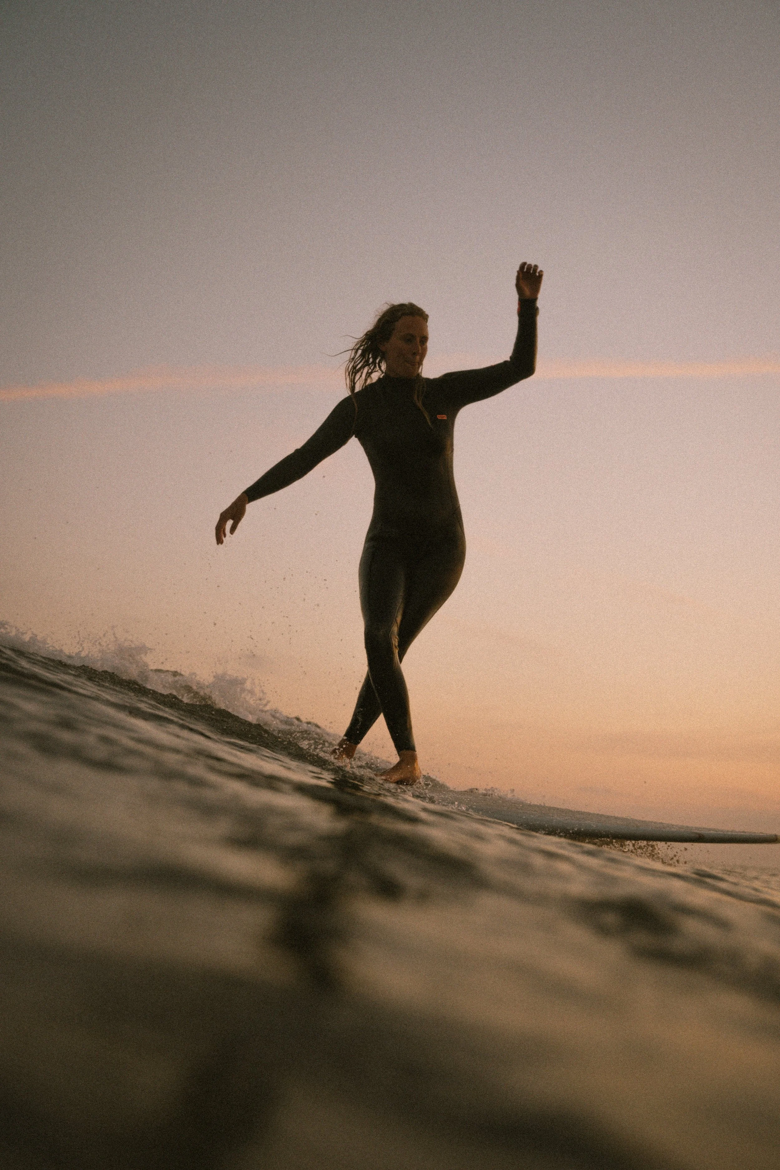 Eine Frau beim Surfen am Strand bei Sonnenuntergang.