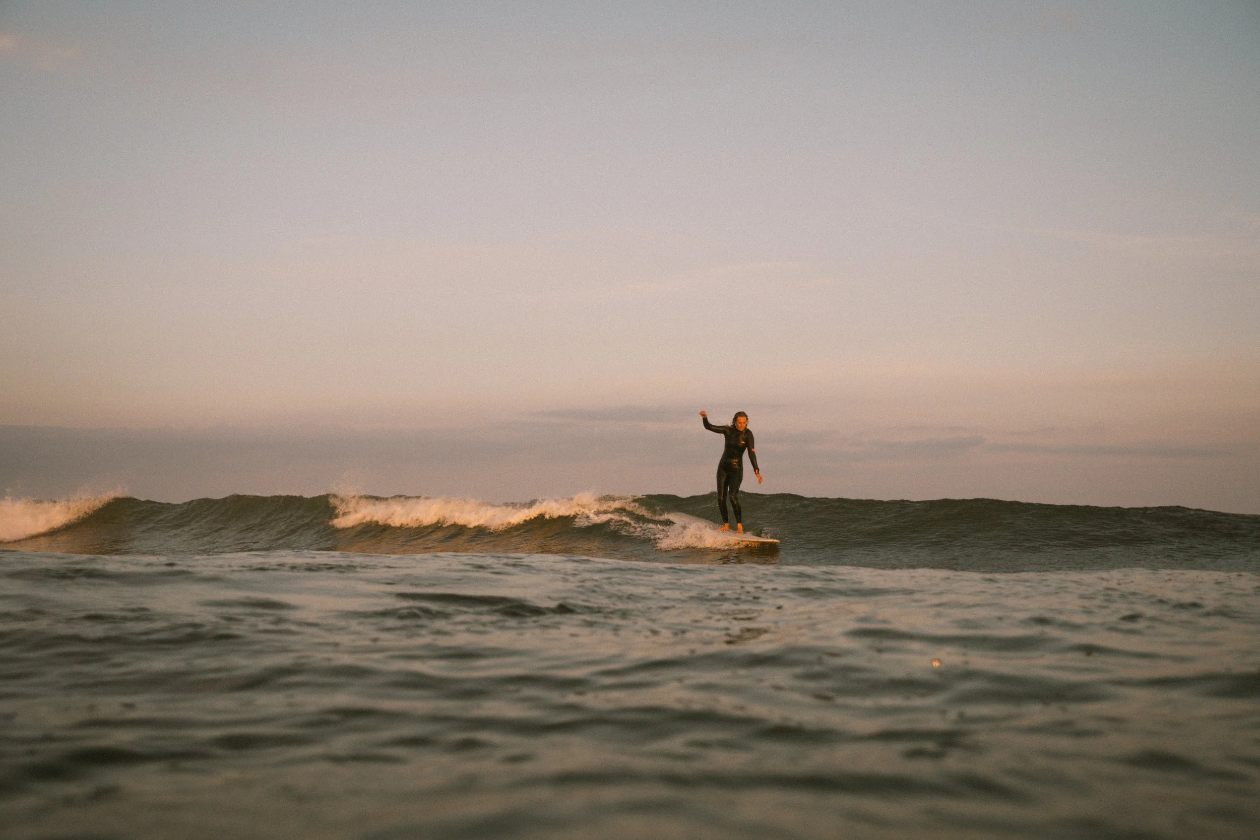 Eine Person beim Surfen auf dem Meer bei Sonnenuntergang.